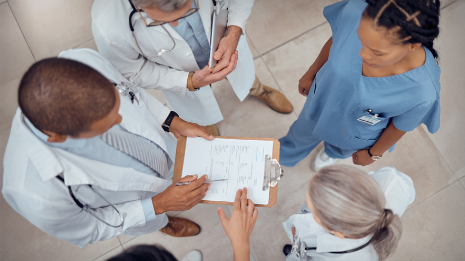 Group of clinicians standing in a circle discussing a document on a clipboard.